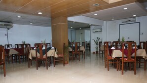 Un salón de conferencias con sillas y mesas de madera, piso de baldosas brillantes y un equipo de aire acondicionado en la pared.