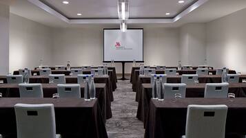 A conference room with multiple tables, each with water bottles and glasses, and a large screen displaying the Marriott Seattle Bellevue logo.