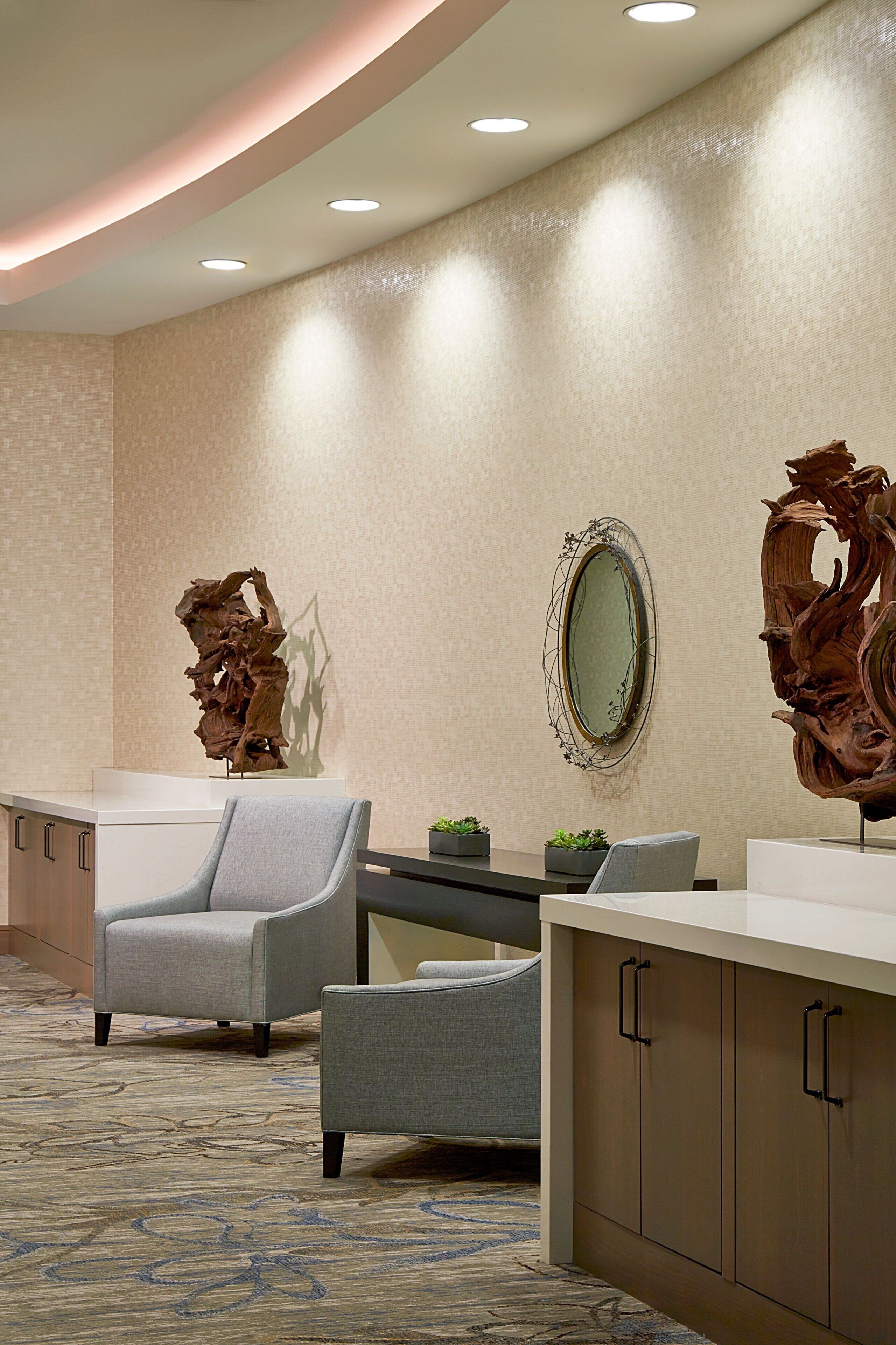 Un hall d’hôtel comprenant un comptoir d’accueil, deux fauteuils, un miroir et des œuvres d’art décoratives murales.