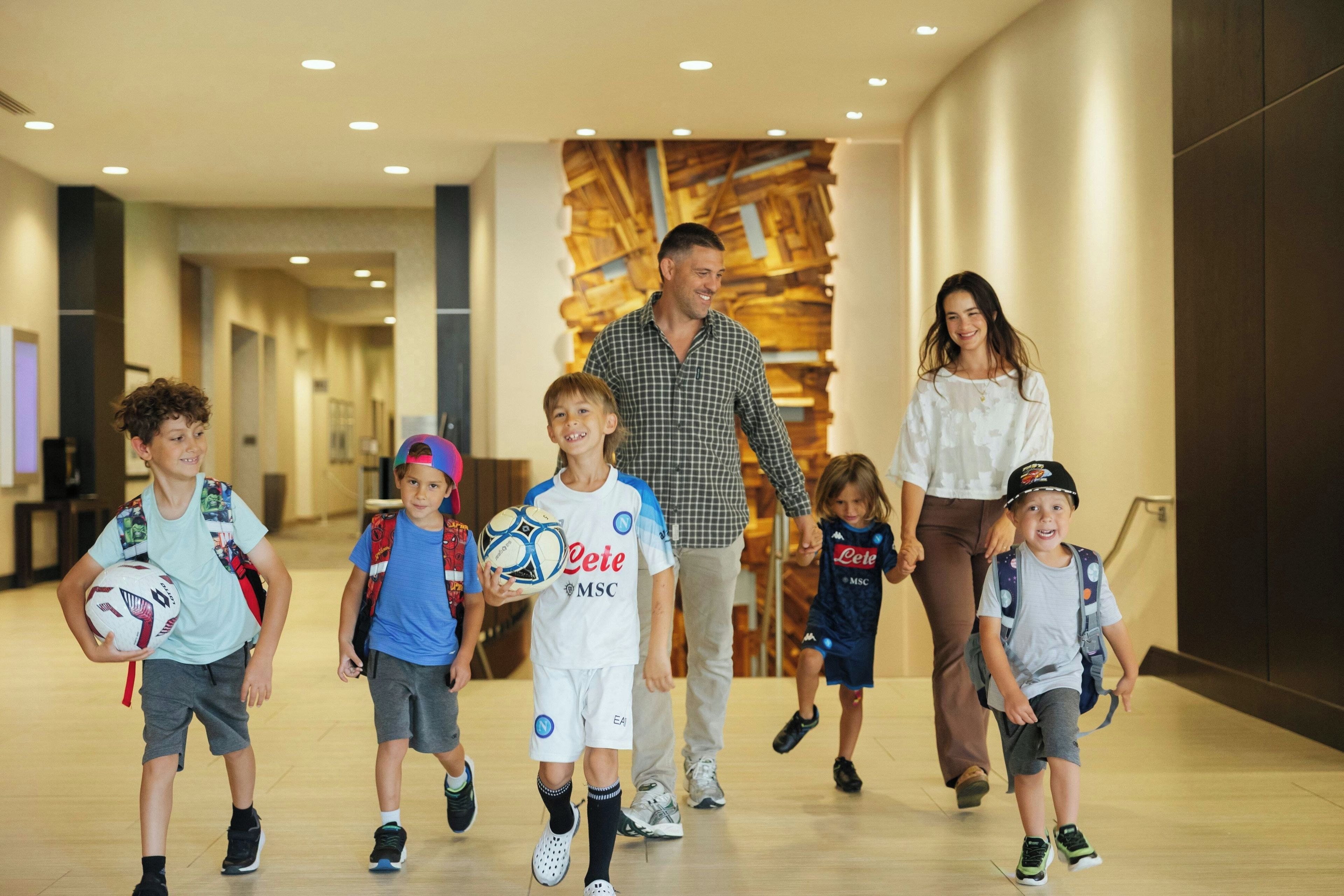 A group of people walking in a hallway with a modern interior design, including a wooden wall and recessed lighting.