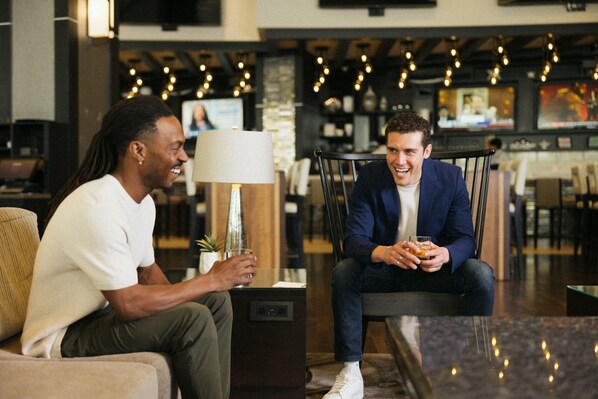 Two people seated in a modern lobby with a bar area in the background. - Seattle Marriott Bellevue (Bellevue)