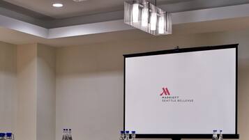 Ein Konferenzraum mit langem Tisch, Stühlen, Wasserflaschen und einem Bildschirm, der das Logo von Marriott Seattle Bellevue zeigt.