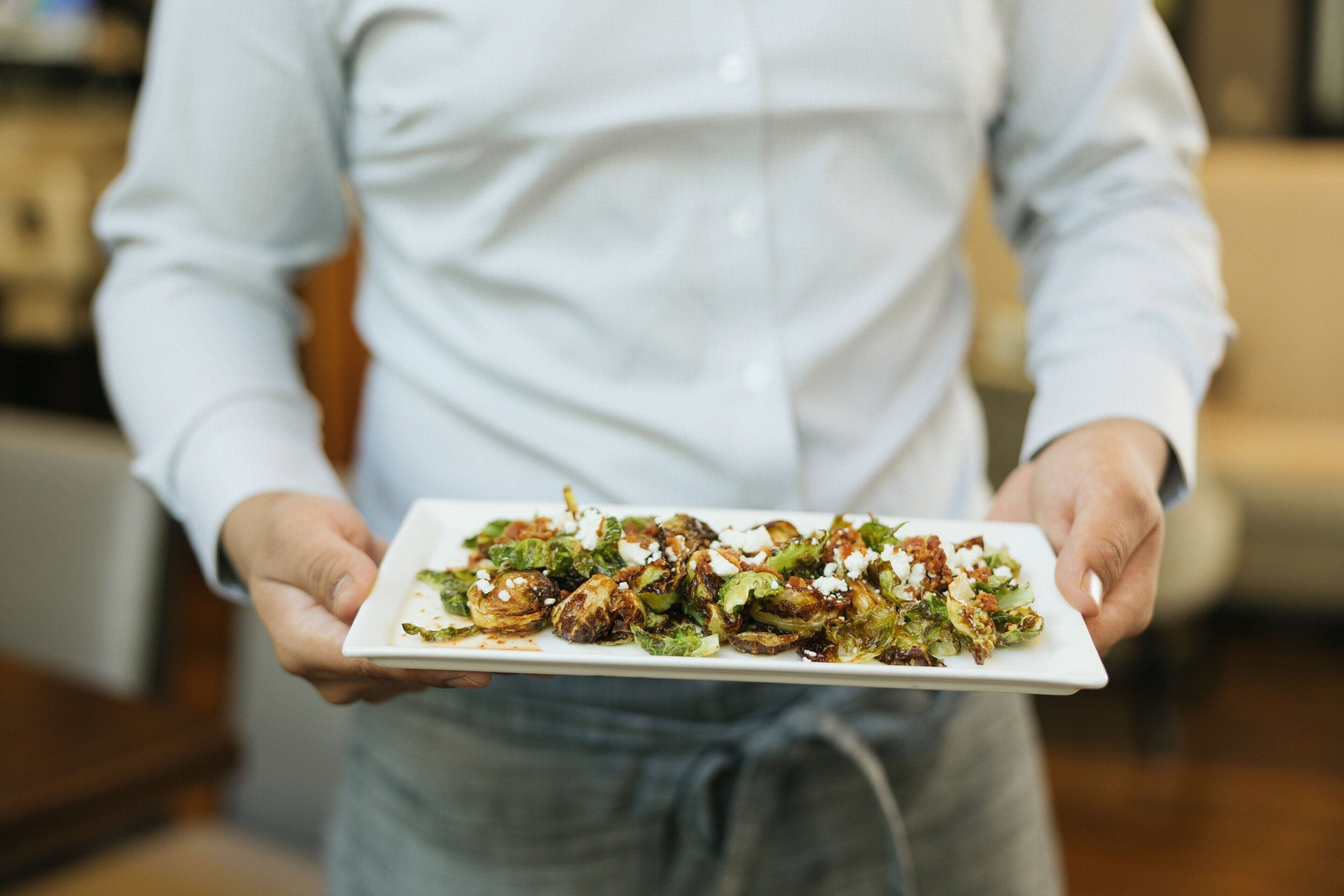 A person holding a rectangular white plate with a food dish.