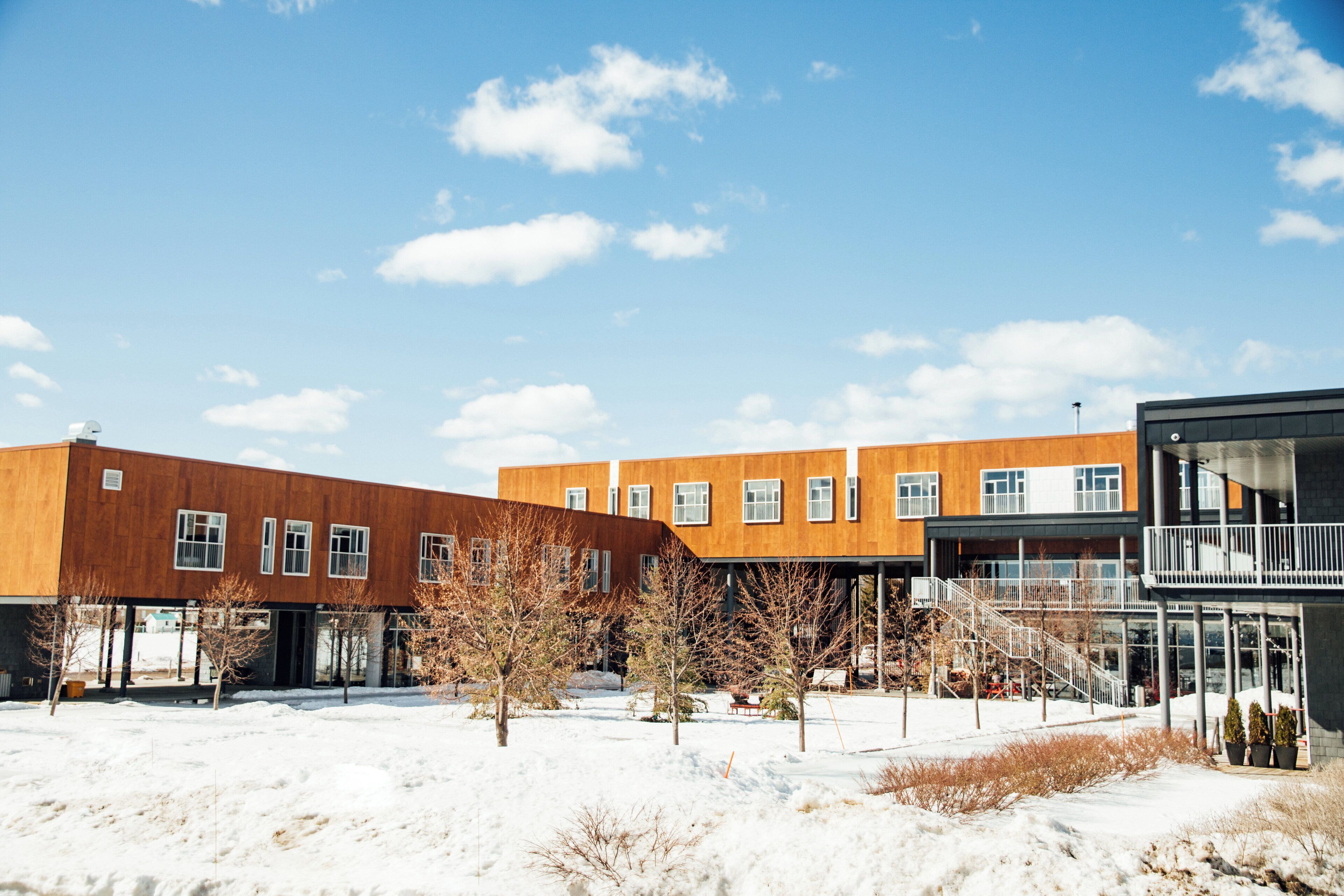 A modern building with a flat roof, large windows, and a covered outdoor area with stairs.