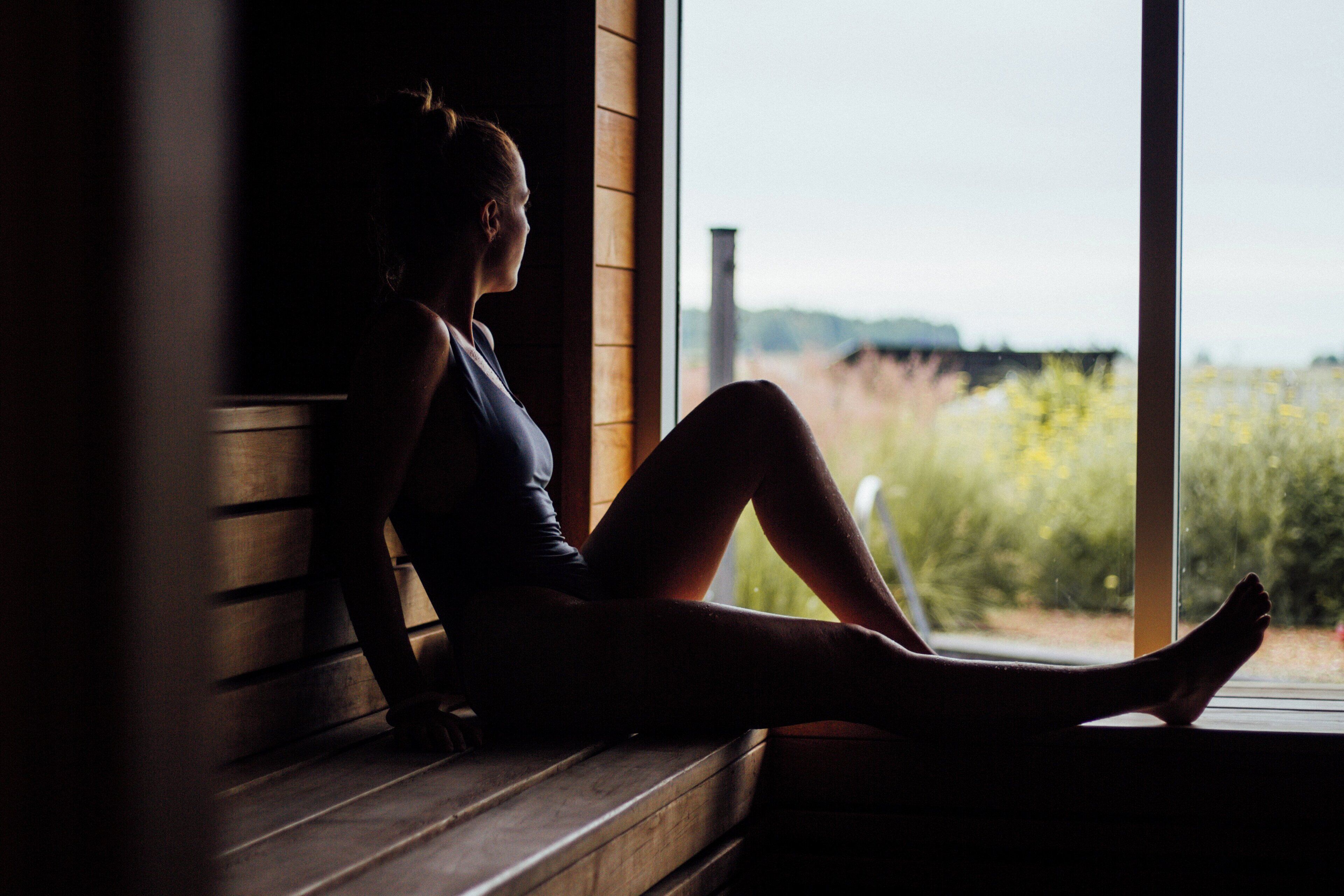 Une personne est assise sur un banc en bois près d’une fenêtre, d’où l’on peut admirer la verdure environnante.