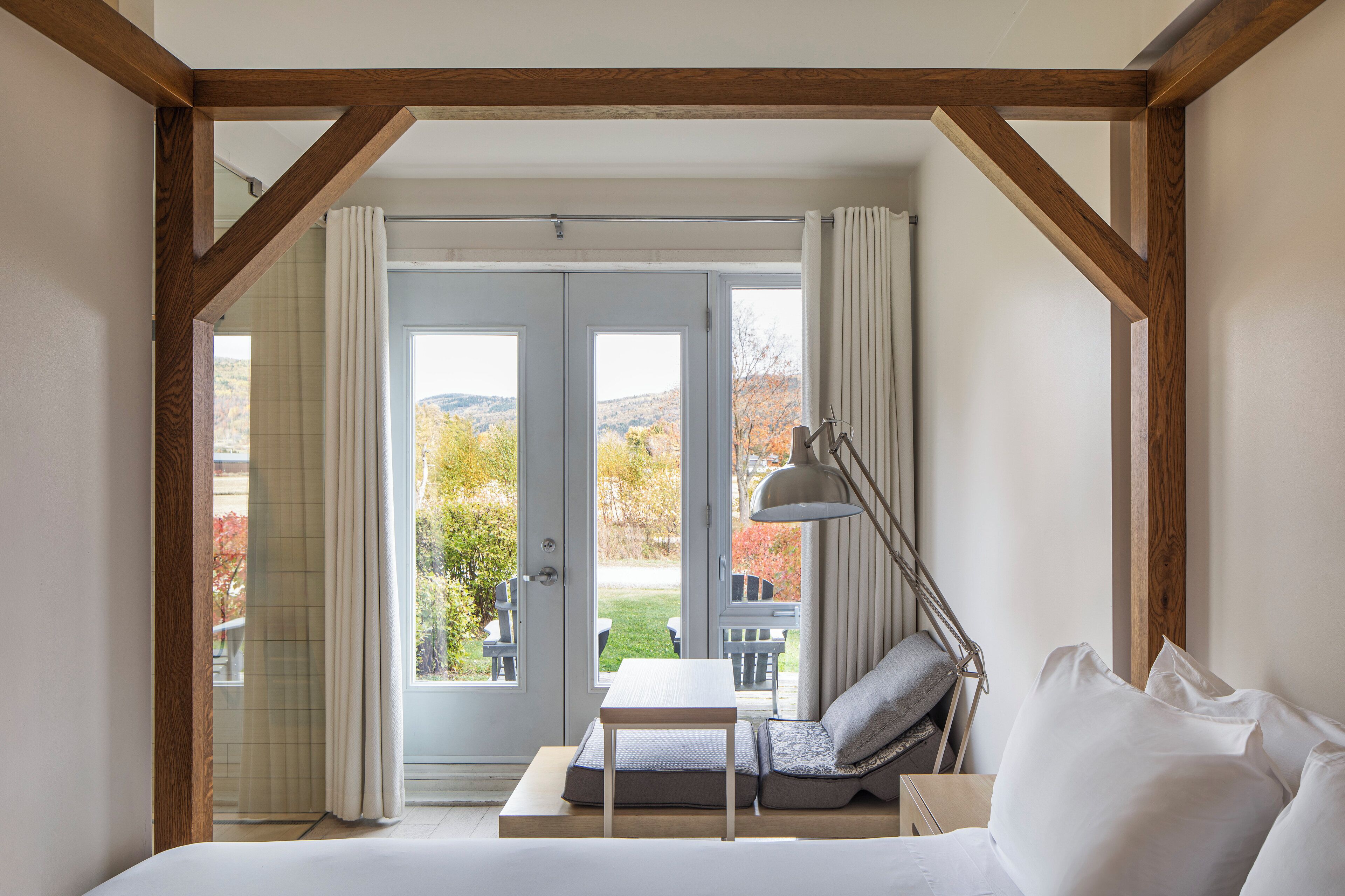 A bedroom with a bed, a bedside table, a lamp, and a view of the outdoors through a glass door.