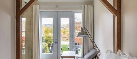 A bedroom with a bed, a bedside table, a lamp, and a view of the outdoors through a glass door.