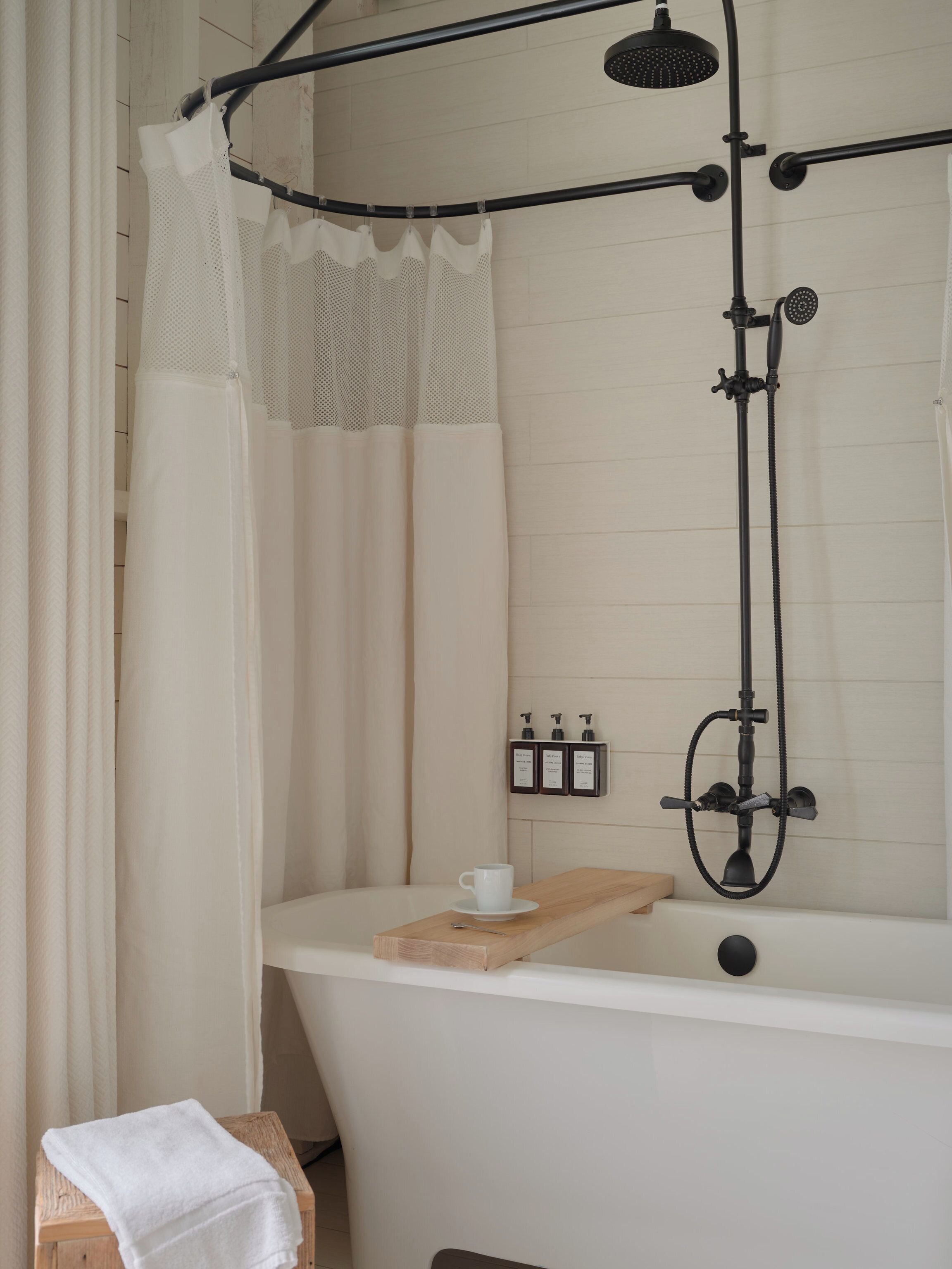 A bathroom with a bathtub, a showerhead, and a cup on a tray.