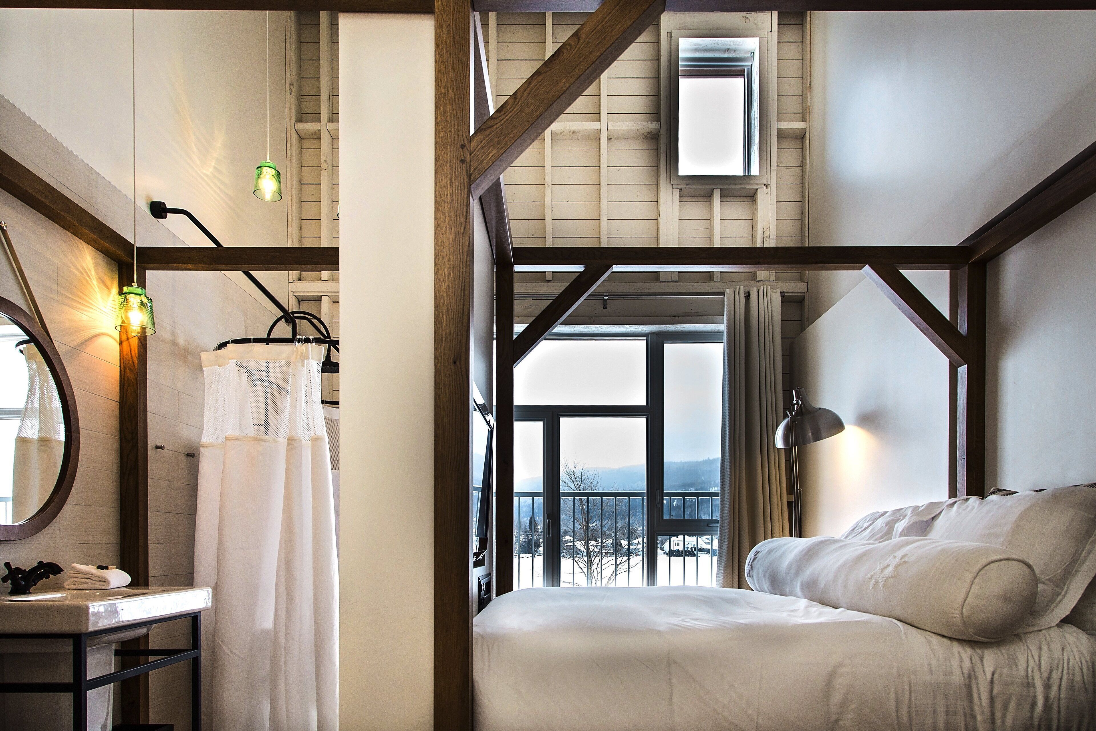 Une chambre avec un grand lit, une table de chevet, un miroir et une vue sur l’extérieur.