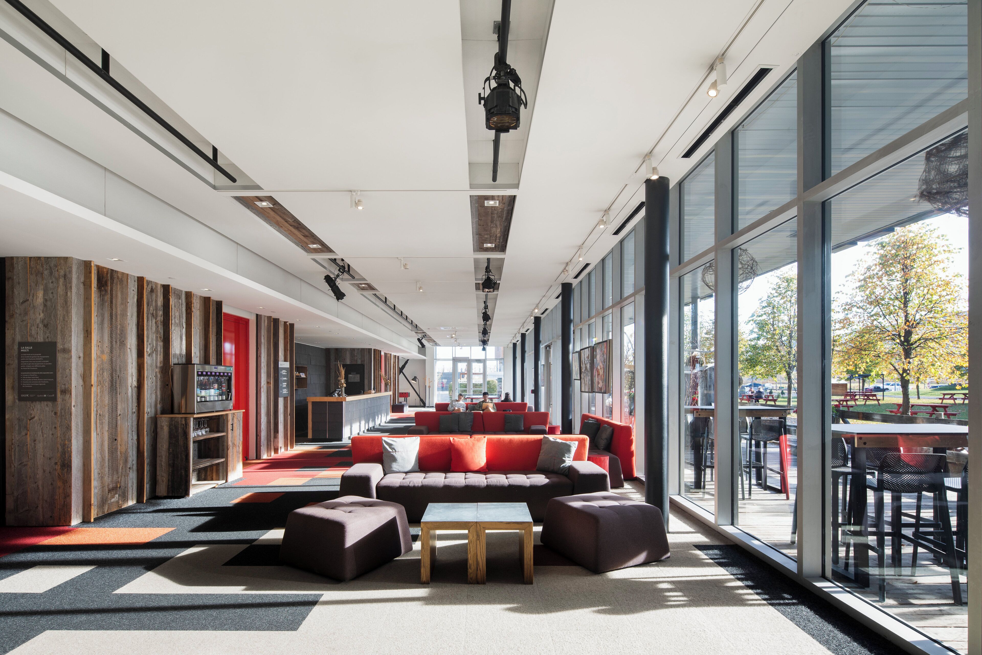 Un espacio interior amplio con un largo banco, asientos rojos y grandes ventanales que ofrecen vistas al exterior.