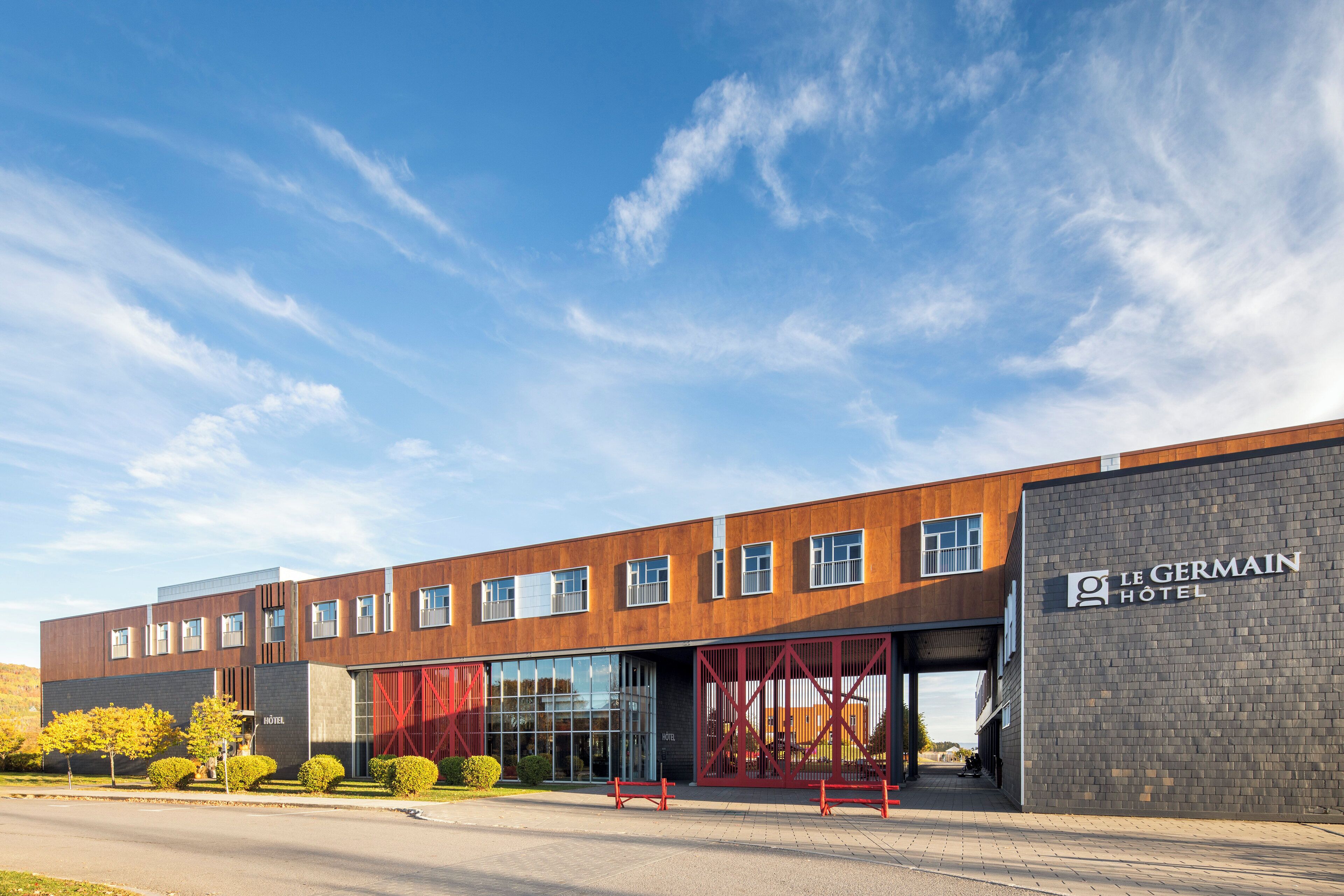 A modern hotel with a large glass facade, a red entrance gate, and a clear blue sky.