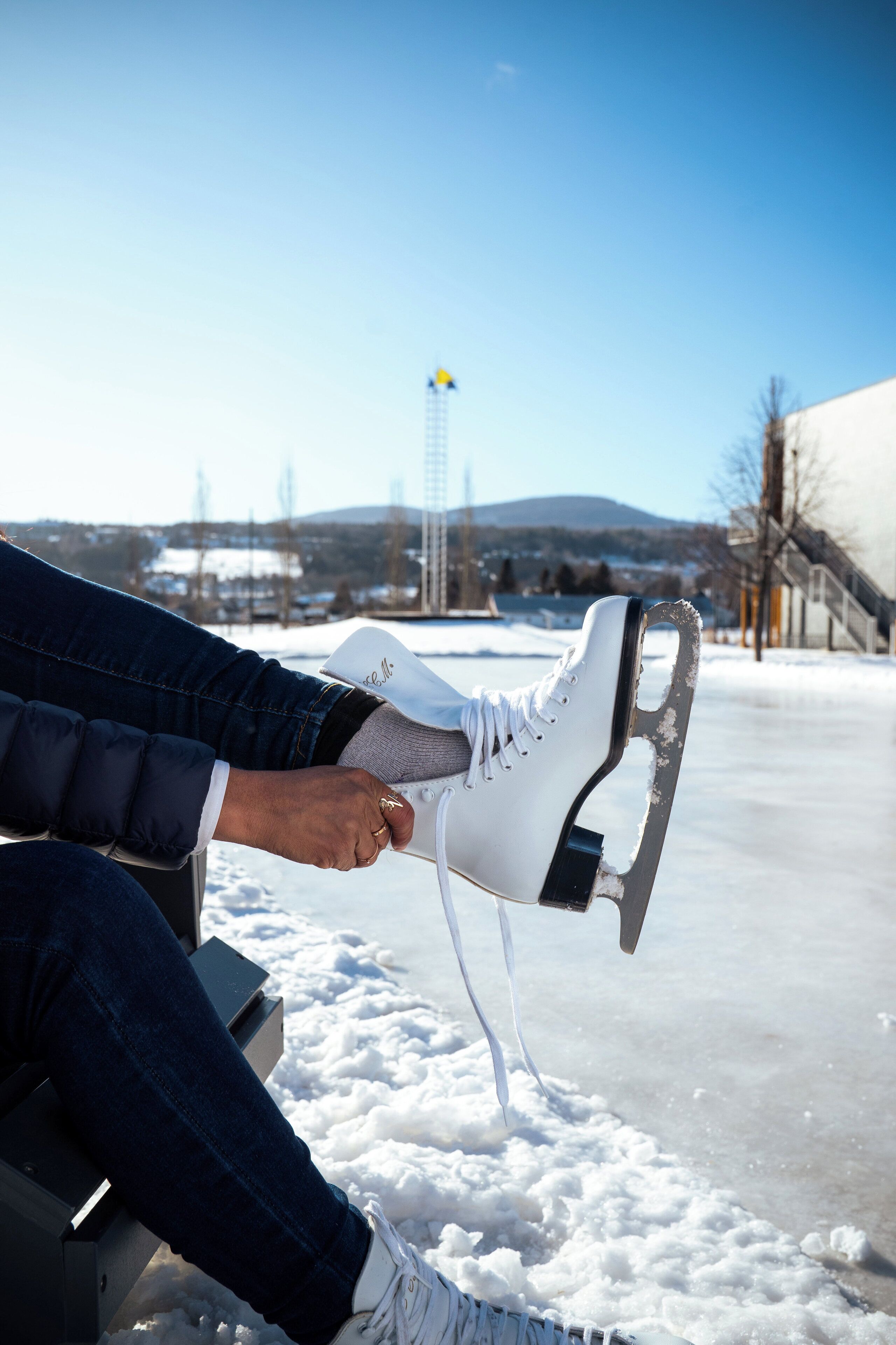 A person sitting on a bench with a pair of ice skates in front of a frozen lake.