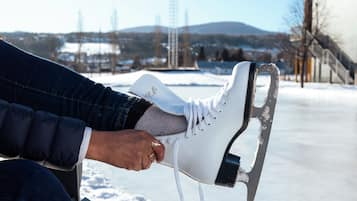 A person sitting on a bench with a pair of ice skates in front of a frozen lake.