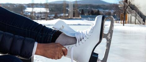 A person sitting on a bench with a pair of ice skates in front of a frozen lake.