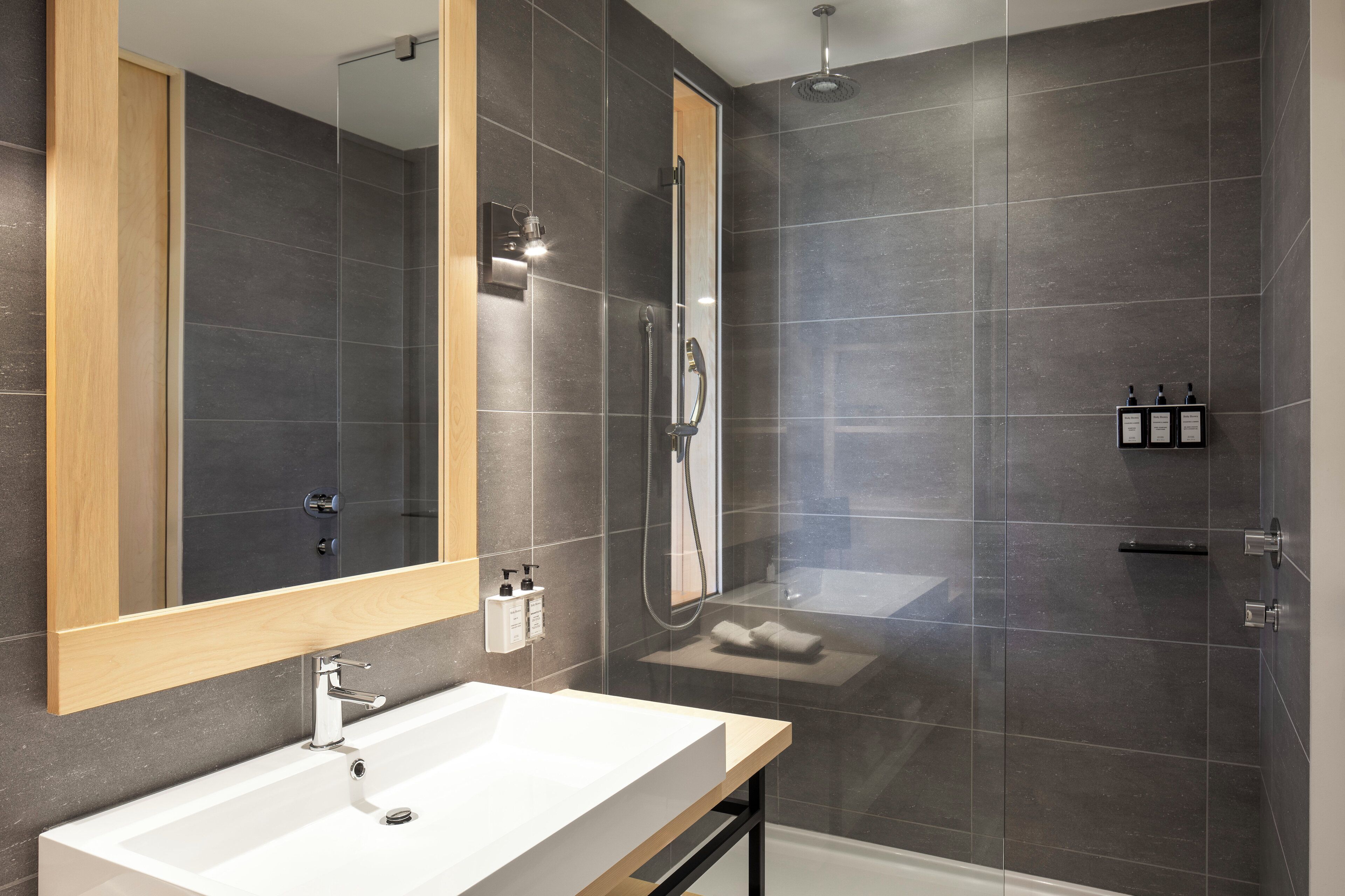 Een moderne badkamer met een grote spiegel, een witte wastafel, een douchecabine en een handdoekrek.