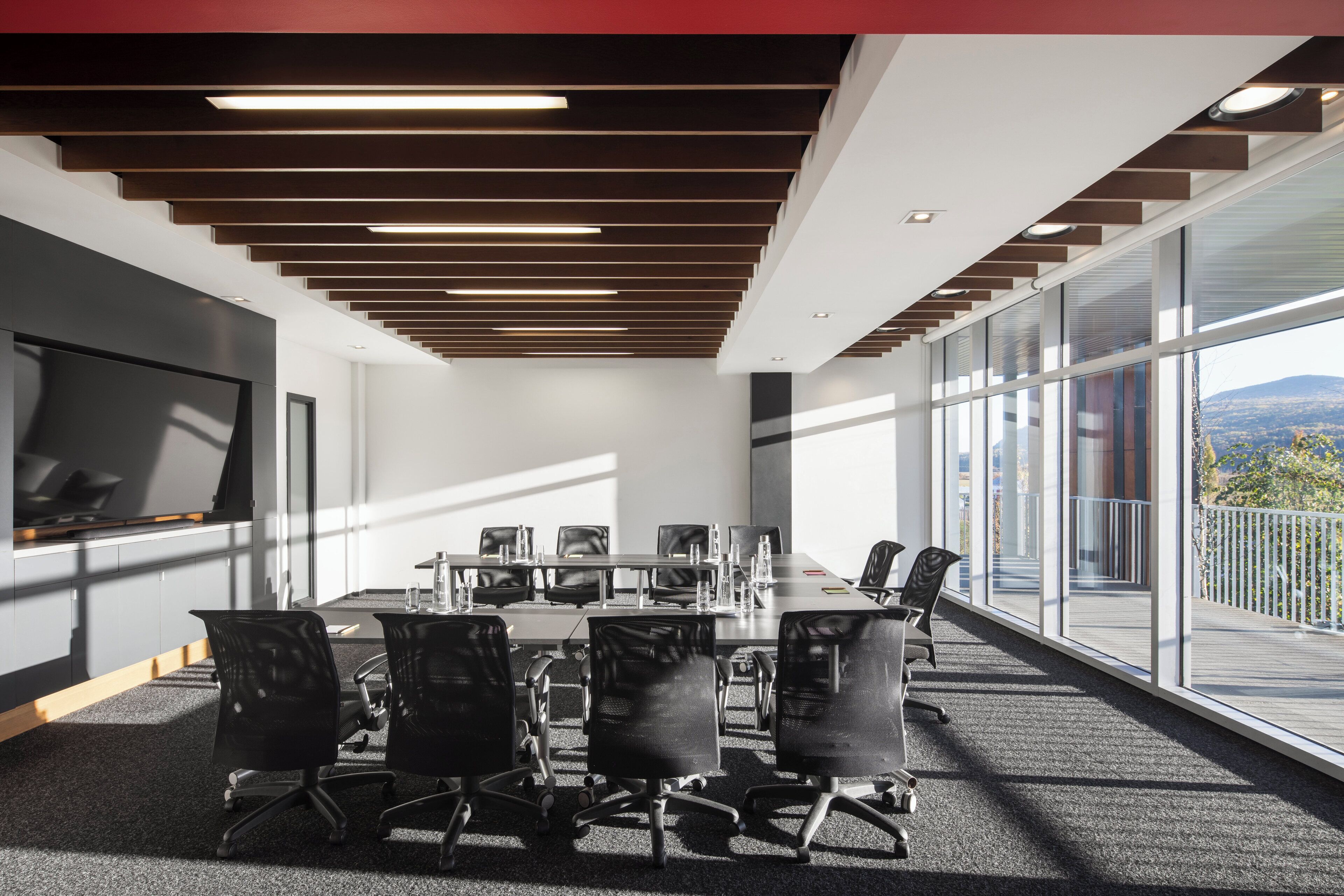 A conference room with a long table, black chairs, and large windows offering a view of the outdoors.