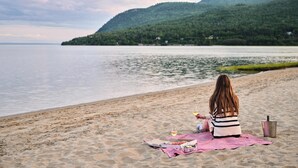 Una persona sentada en la playa con un montaje de picnic, que incluye una manta, comida y bebidas.