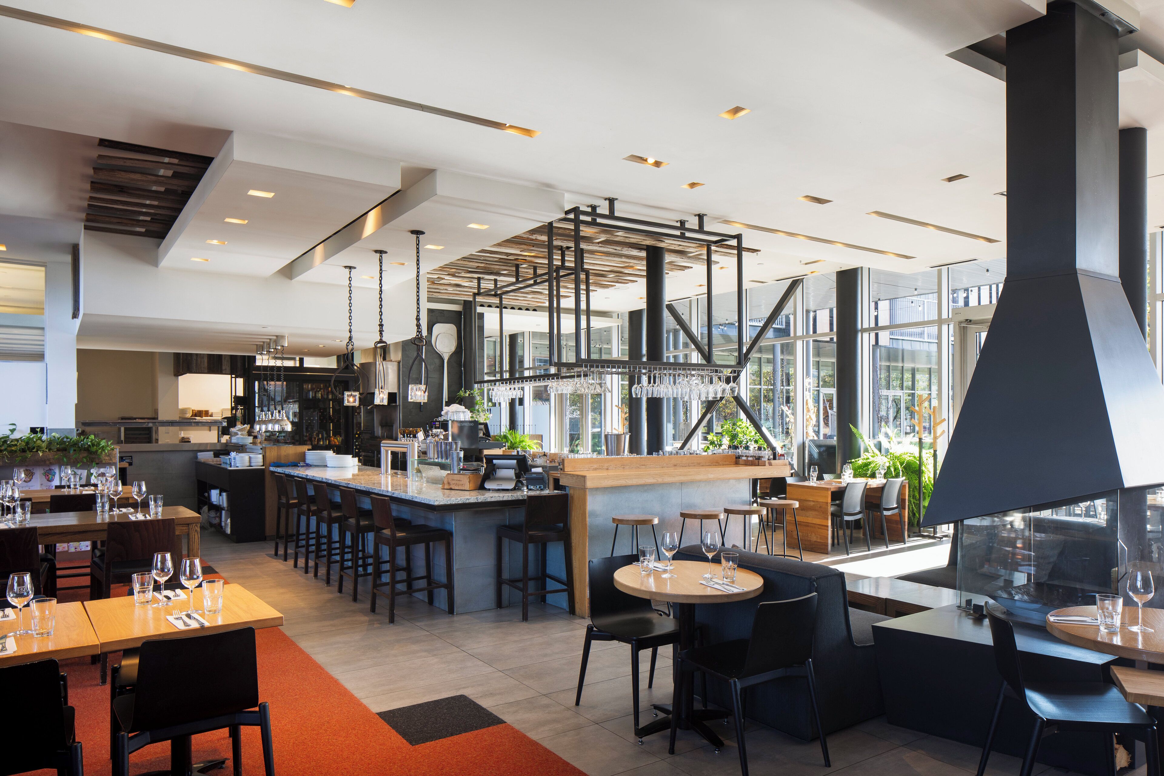 Een modern restaurant met een bar, hoge plafonds en grote ramen.