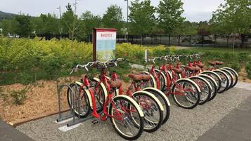 A bike-sharing station with multiple red bicycles and a sign labeled "BAJECYCLE".