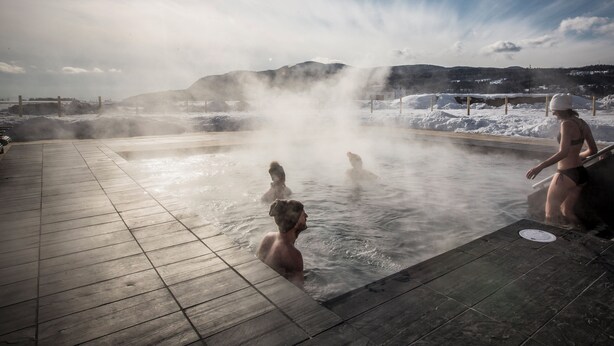 Un spa geotérmico con aguas termales, una terraza de madera y un telón de fondo montañoso.