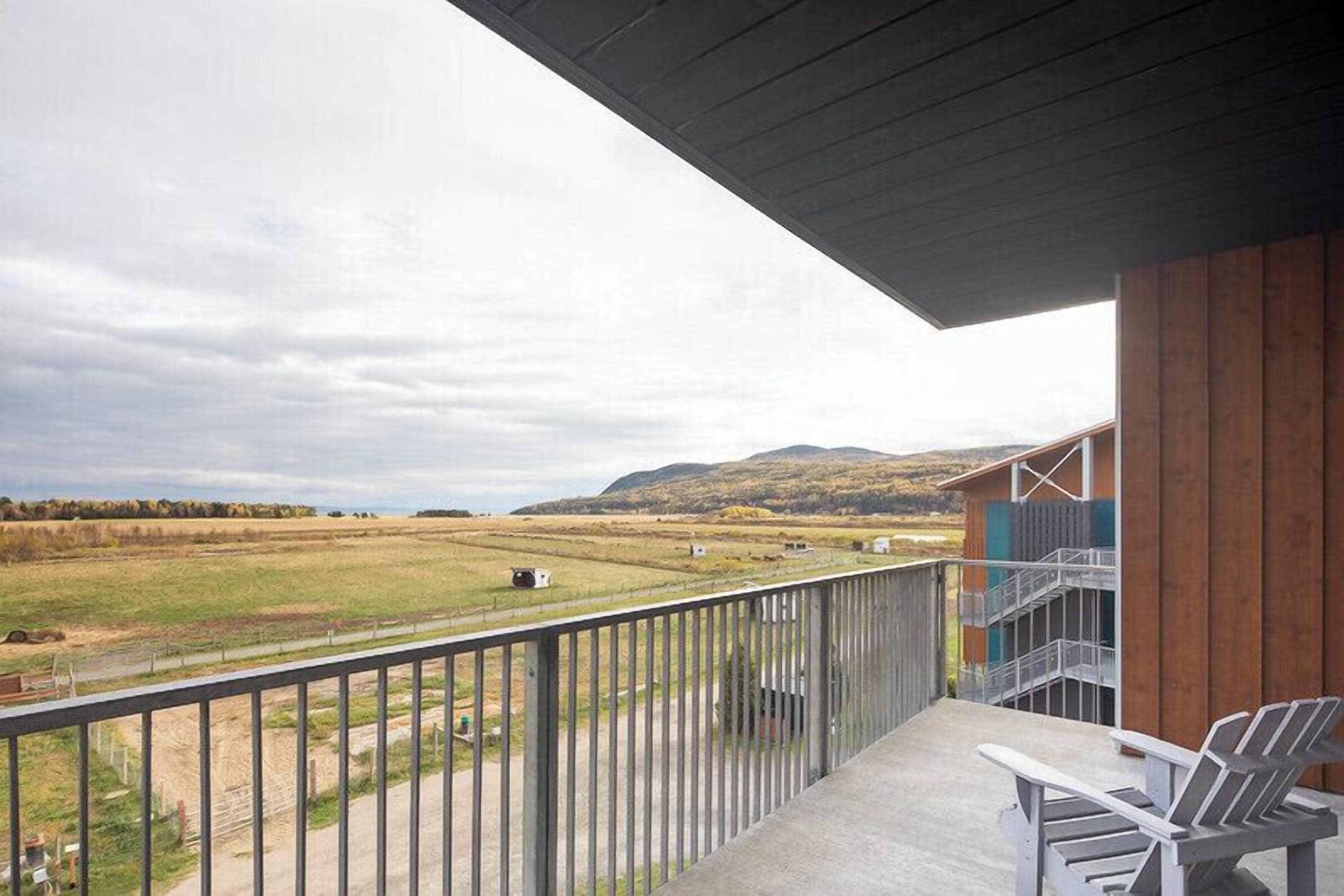 Un balcon donnant sur un paysage rural, un bâtiment en bois et une chaise.