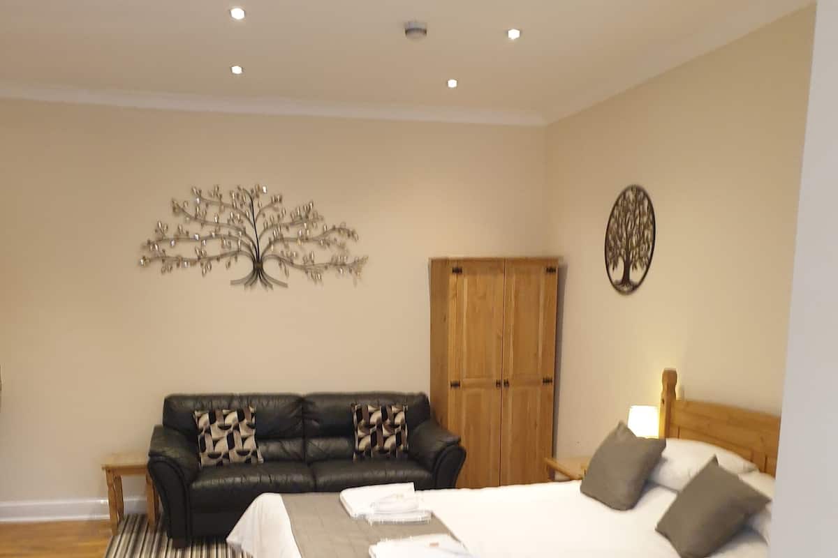 A bedroom with a bed, a sofa, a wardrobe, and a decorative tree wall art.