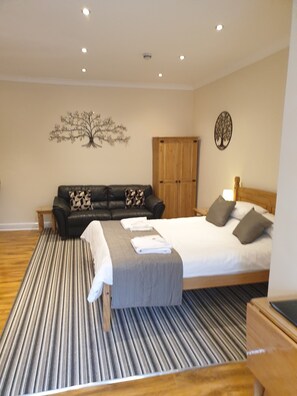 A bedroom with a bed, a sofa, a wardrobe, and a decorative tree wall art. - Appletorre House Holiday Flats (Torquay)