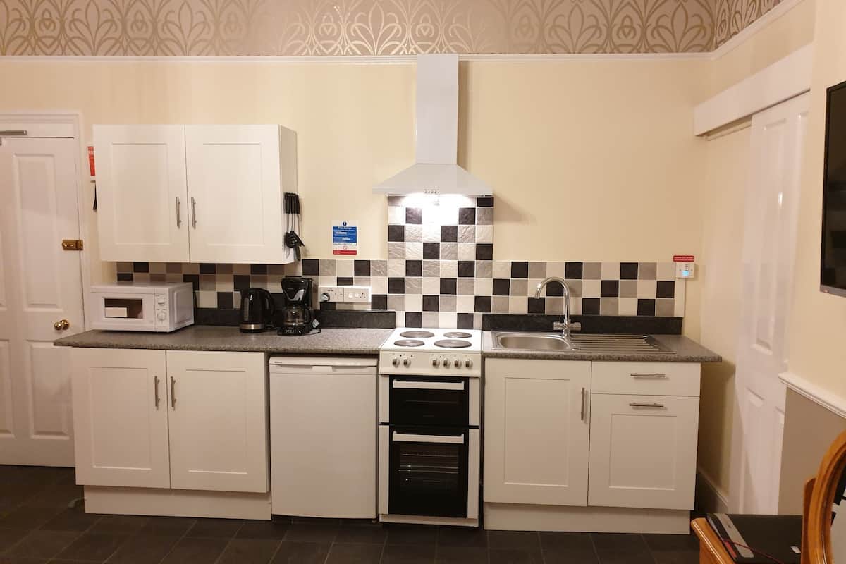 A compact kitchen with white cabinets, a microwave, a coffee maker, a stove, and a sink.