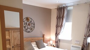 A neatly made bed with a grey and white duvet, a wooden headboard, and a bedside table with a lamp. - Appletorre House Holiday Flats (Torquay)
