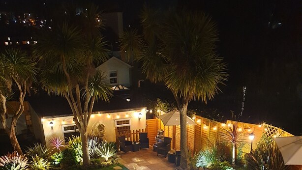 A well-lit outdoor patio area with a pool, seating, and a wooden deck. - Appletorre House Holiday Flats (Torquay)