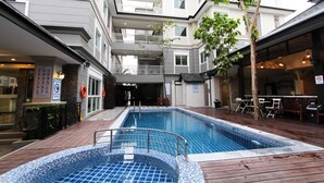 A swimming pool with a tiled deck, surrounded by a multi-story building with balconies and outdoor seating.