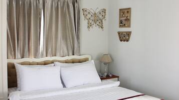 A neatly made bed with white bedding and a red trim, a bedside table with a lamp, and a wall-mounted air conditioner.