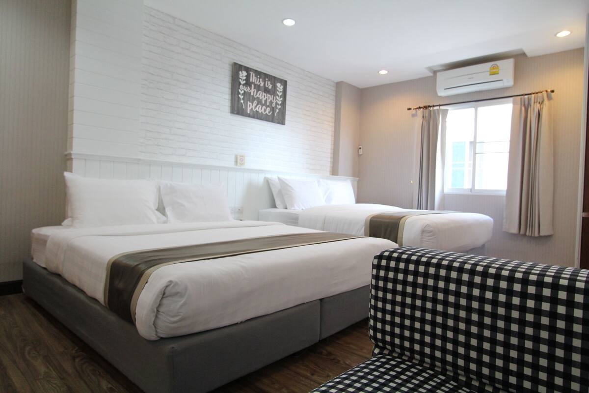 A hotel room with two beds, a checkered chair, and a wall-mounted air conditioner.
