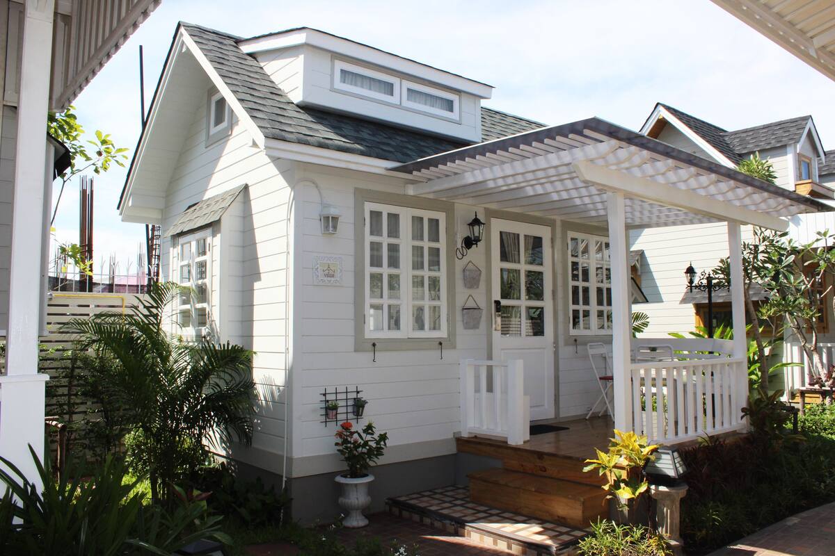 A white house with a covered porch, a small front yard, and a potted plant.