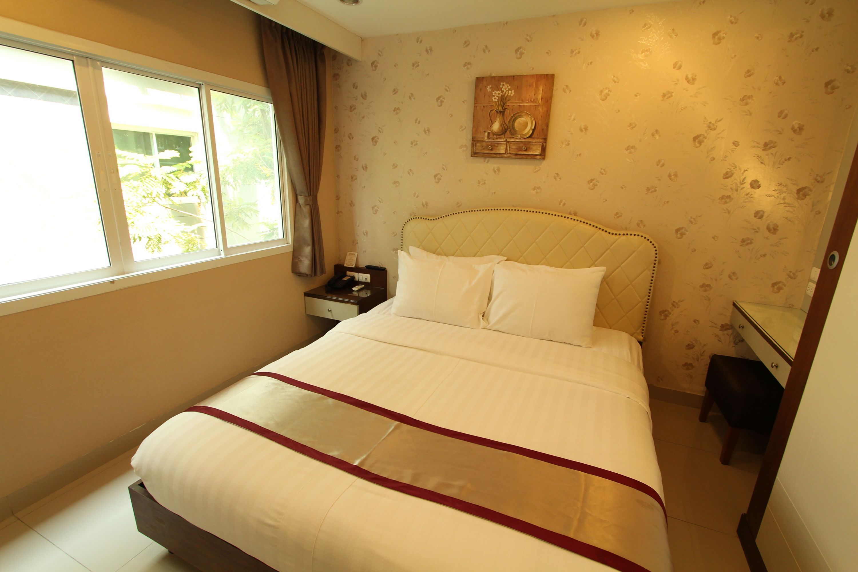A hotel room with a large bed, a nightstand, a desk, and a window with curtains.