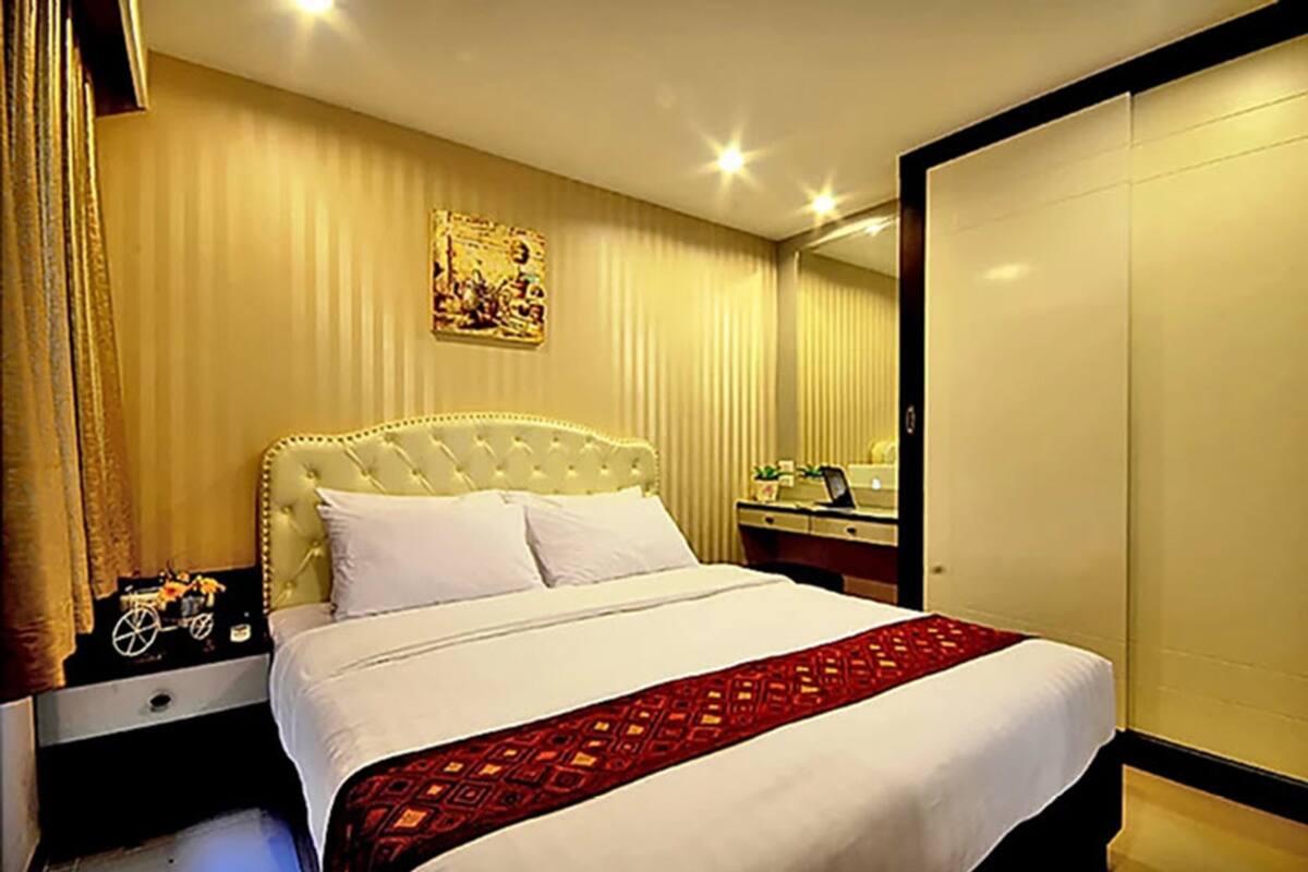 A hotel room with a large bed, a nightstand, a desk, and a wardrobe.