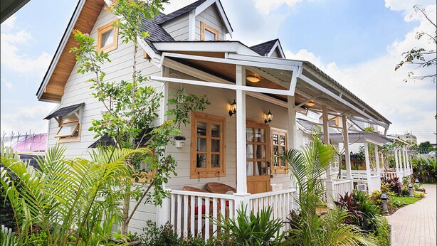 A two-story house with a porch, surrounded by lush greenery.