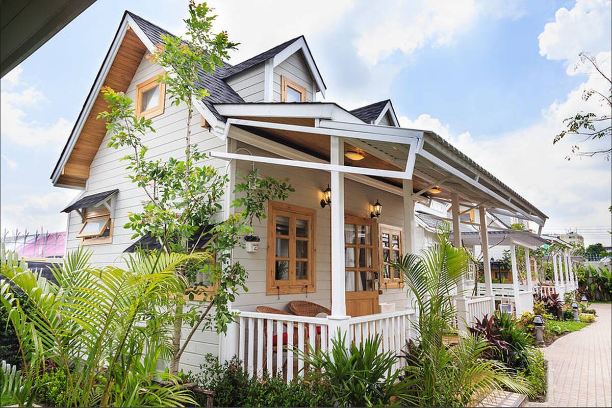 A two-story house with a porch, surrounded by lush greenery.