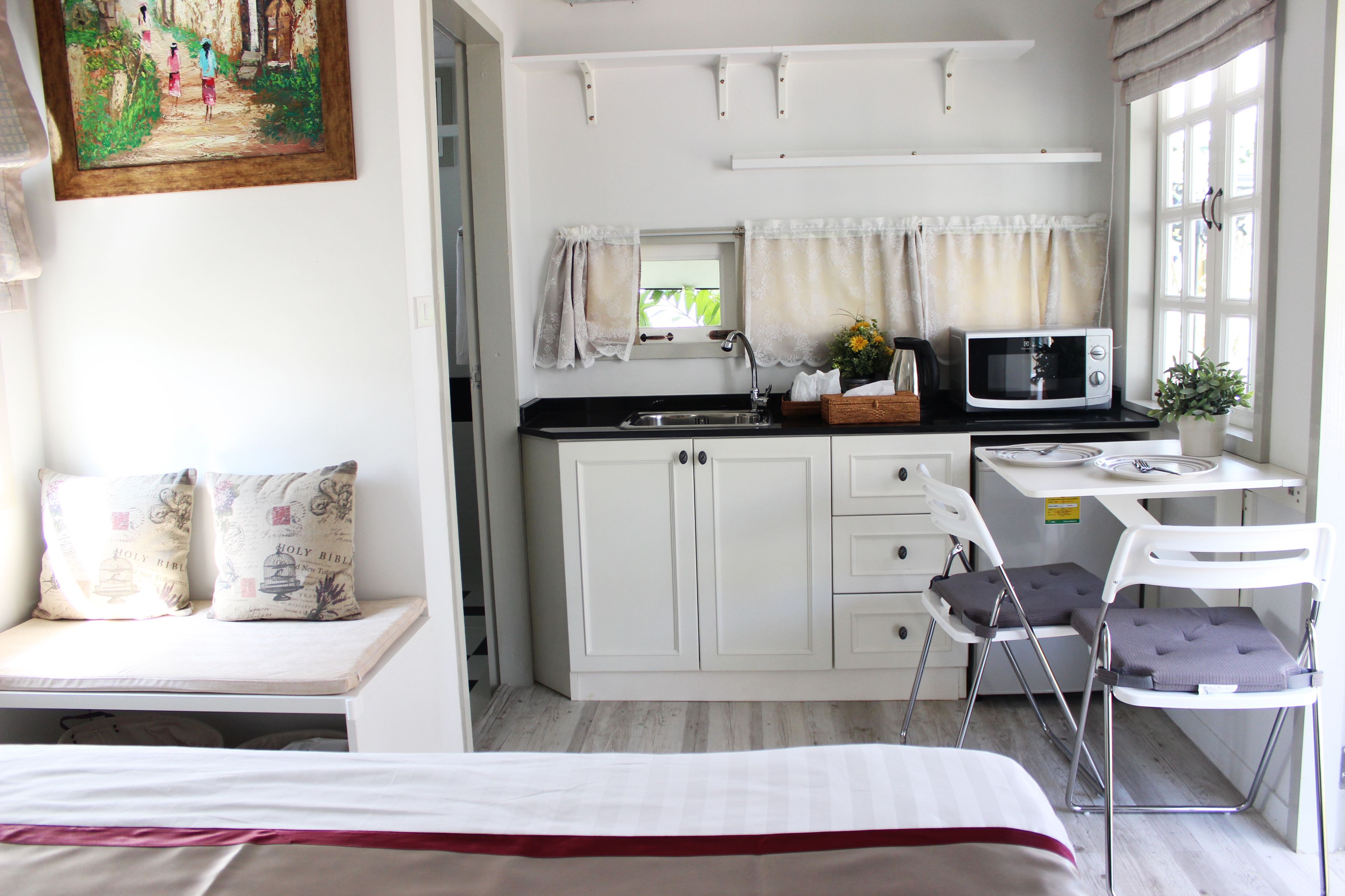 Una habitación compacta con cama, una kitchenette pequeña, un comedor y una ventana con cortinas.