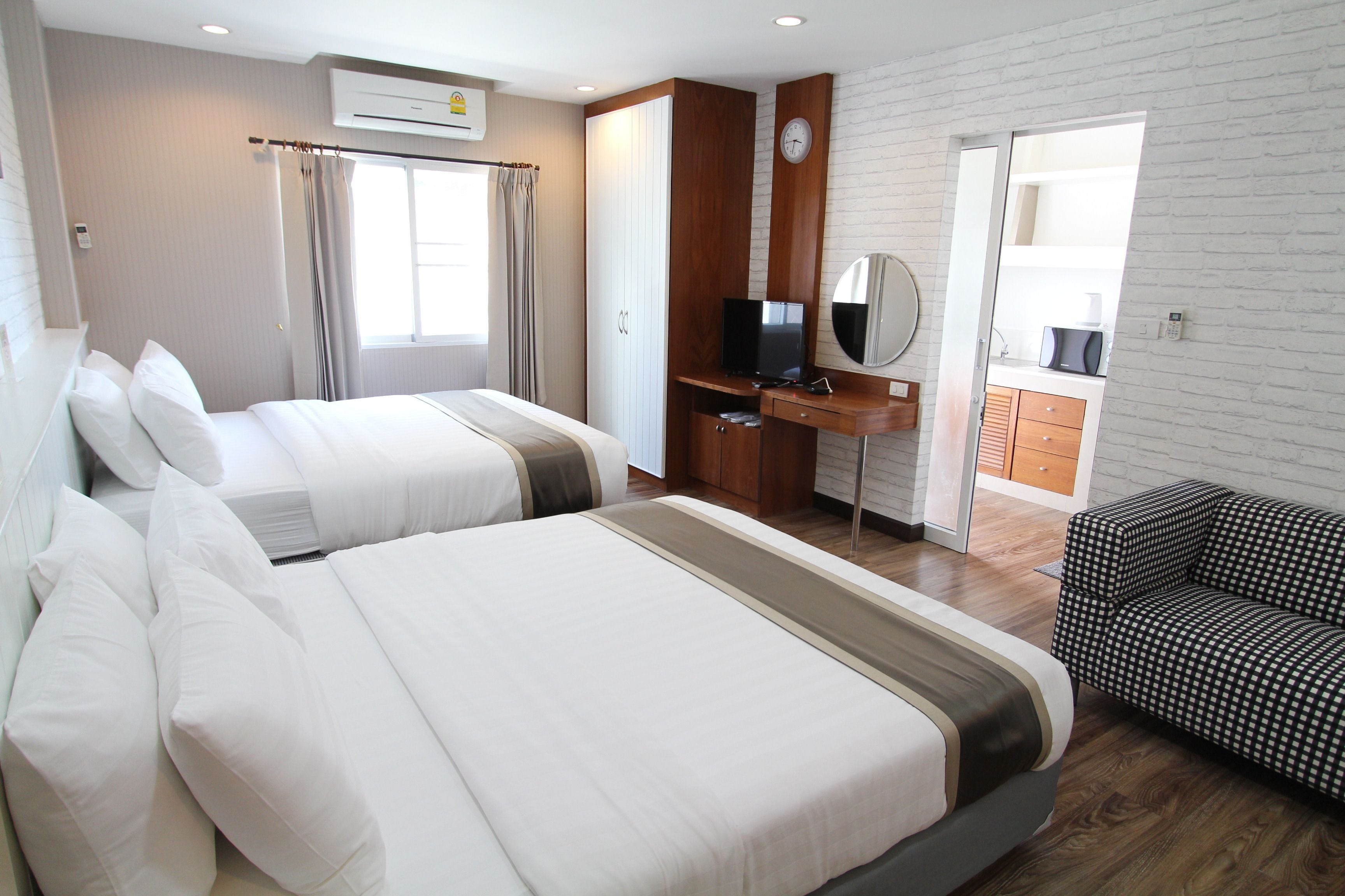 A hotel room with two beds, a desk with a TV, a mirror, and a patterned sofa.
