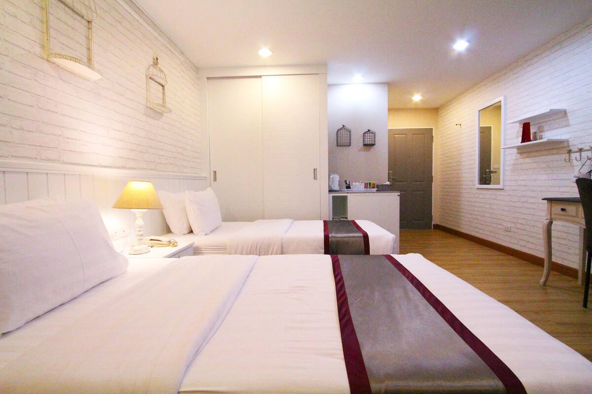 A hotel room with two beds, a small desk, a mirror, and a white brick wall.