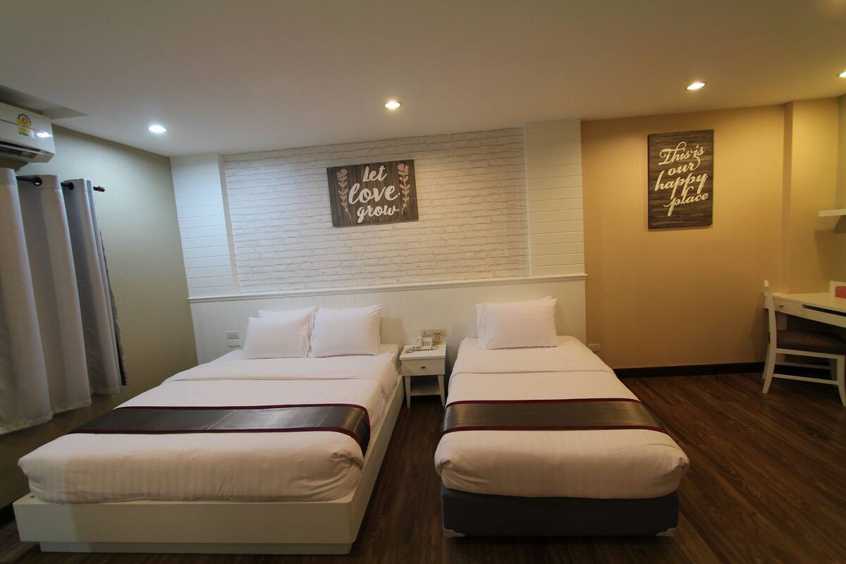 A hotel room with two beds, a small table, and a chair. There are two signs on the wall, one saying "Let love grow" and the other "This is our happy place."
