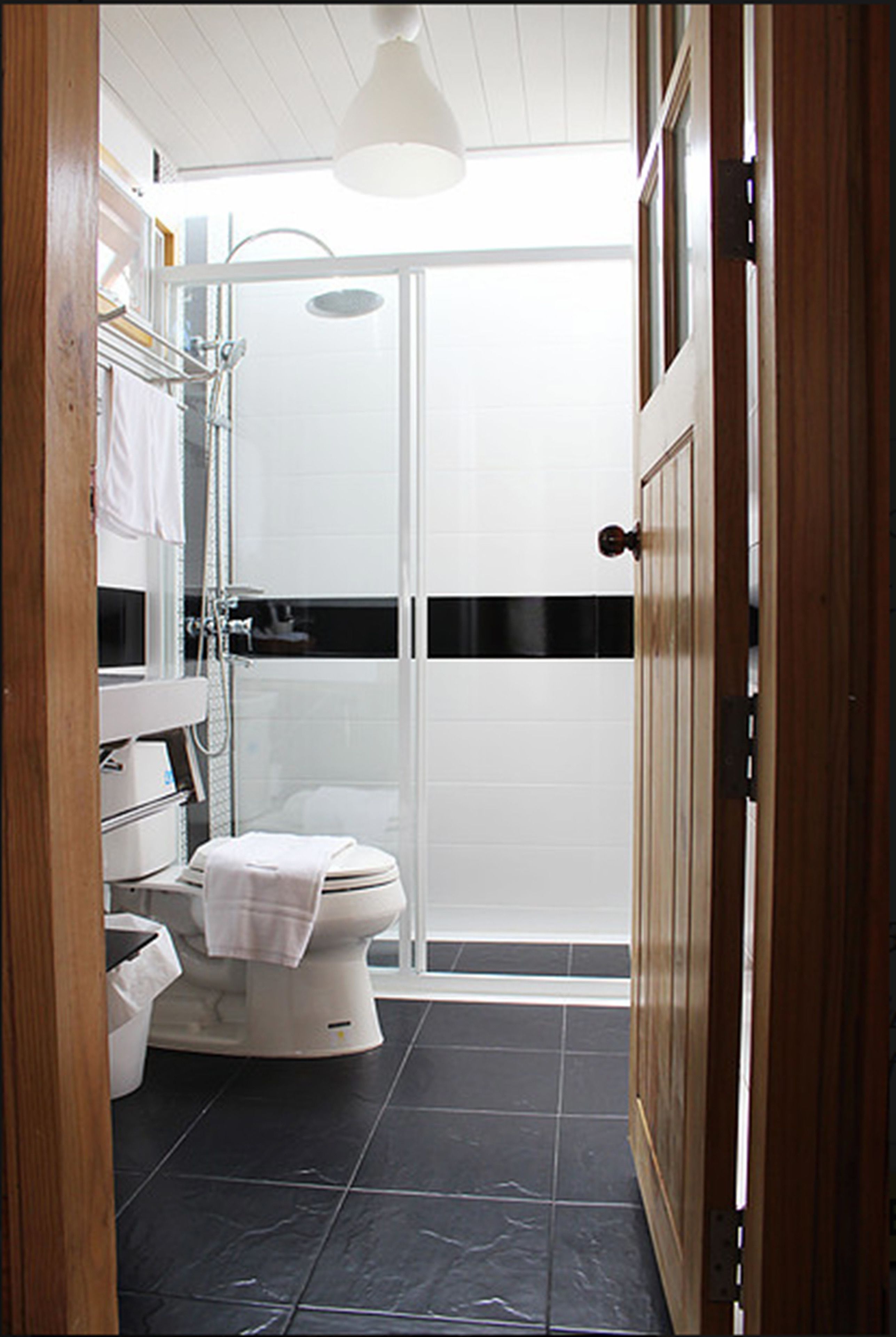 Un baño moderno con cabina de ducha de vidrio, un inodoro blanco y una puerta de madera.