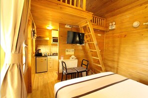 A compact cabin with a bed, a desk, a chair, a television, and a kitchenette.