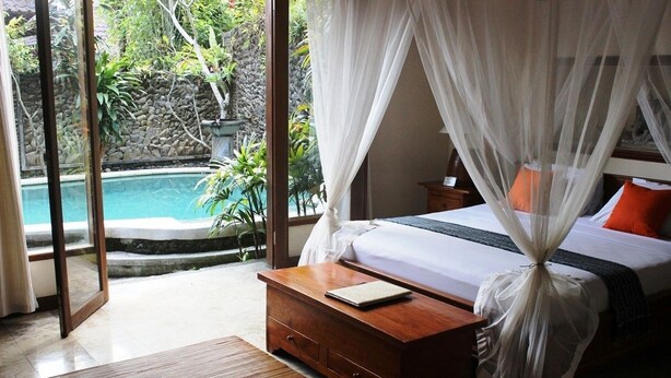 A bedroom with a bed, bedside table, and a view of a swimming pool. - Nefatari Exclusive Villas (Ubud)