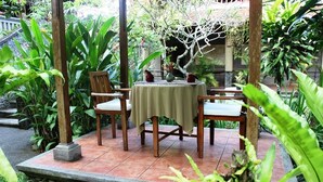 A covered outdoor seating area with a table and chairs, surrounded by lush greenery and a stone pathway. - Nefatari Exclusive Villas (Ubud)