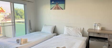 A hotel room with two beds, a small desk, a refrigerator, and a painting of a pier.