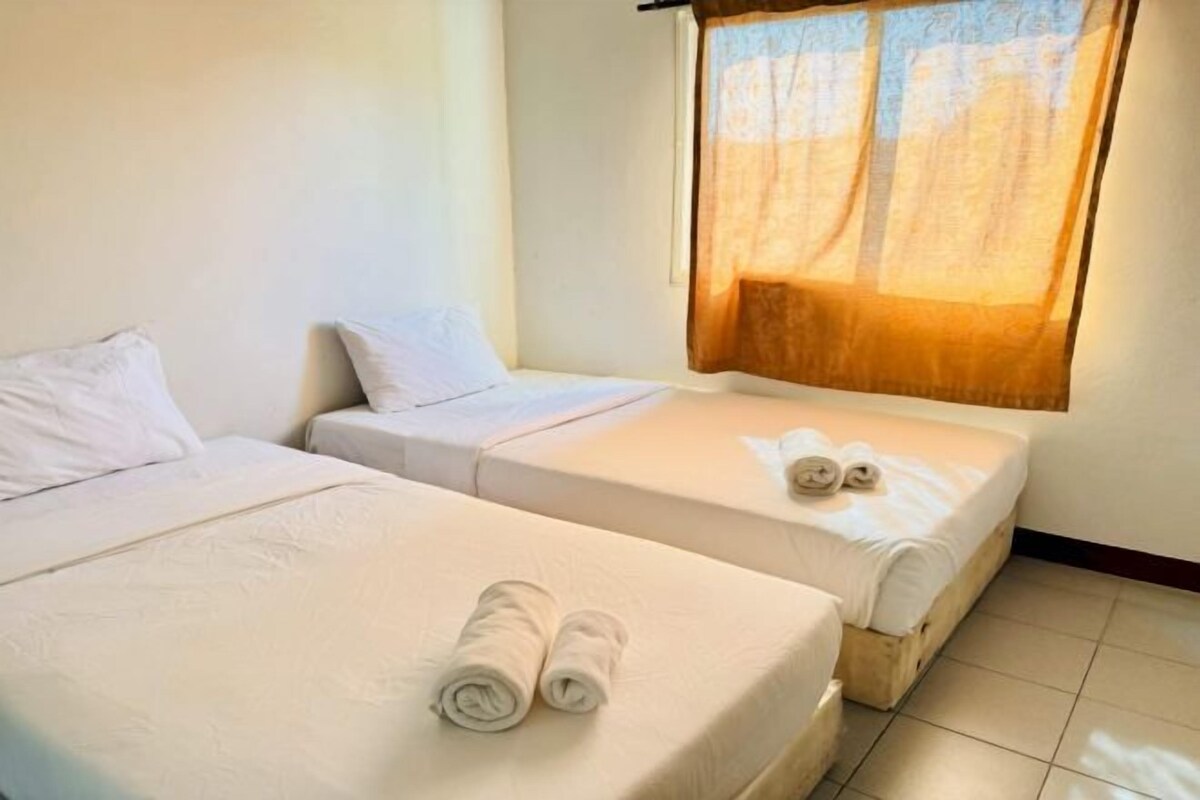 Una habitación de hotel con dos camas, una ventana con cortina translúcida y toallas enrolladas sobre las camas.