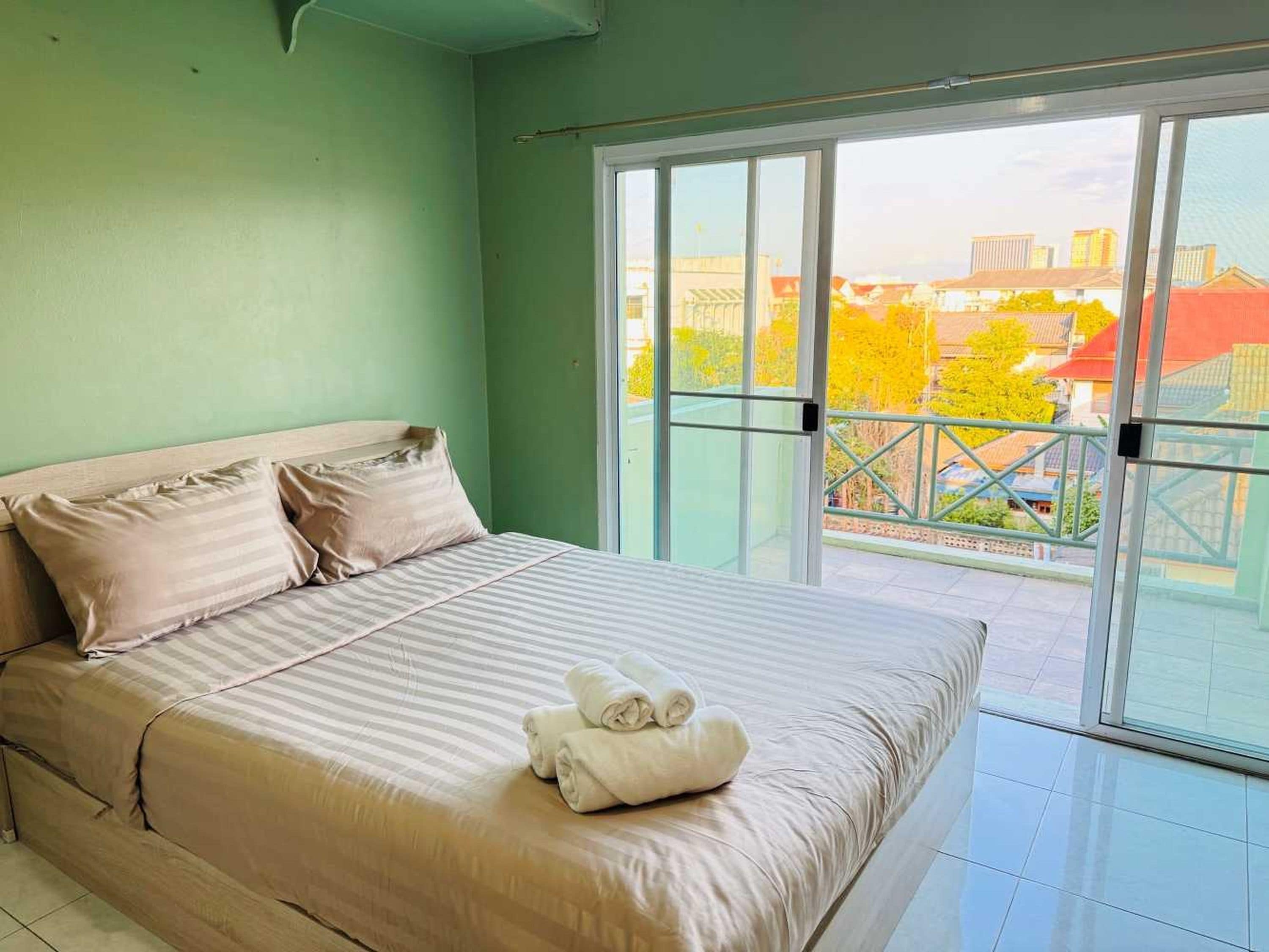 A bedroom with a bed, pillows, and a view of buildings through large windows.