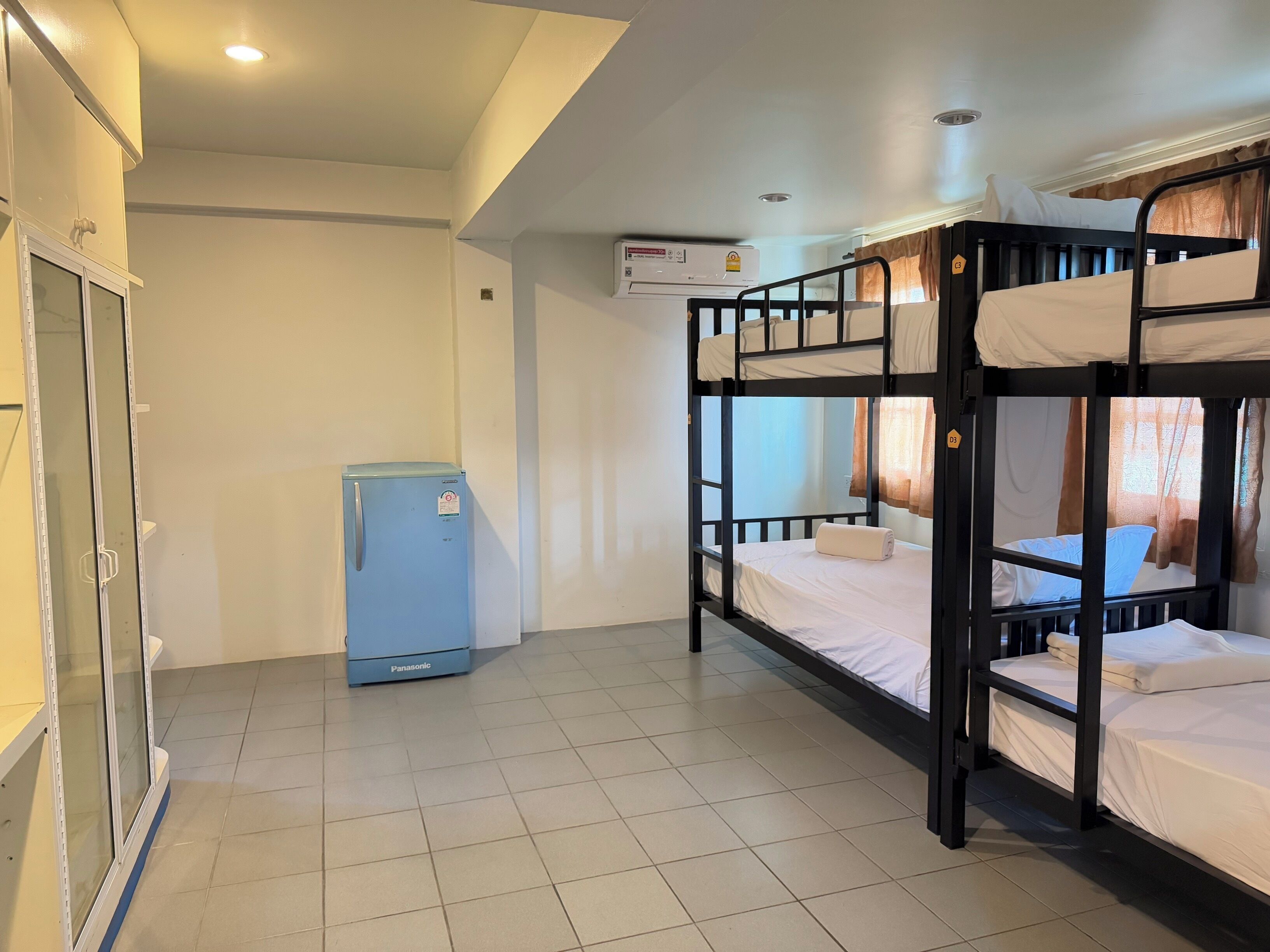 A dormitory room with bunk beds, a refrigerator, and a window with curtains.